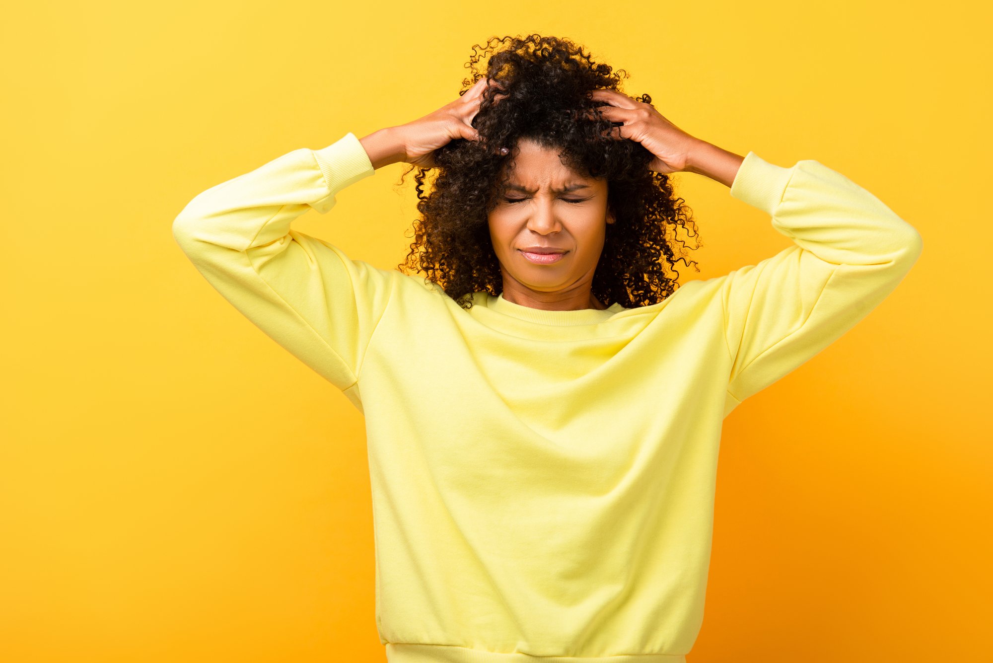 African american woman with closed eyes fixing curly hair on yellow