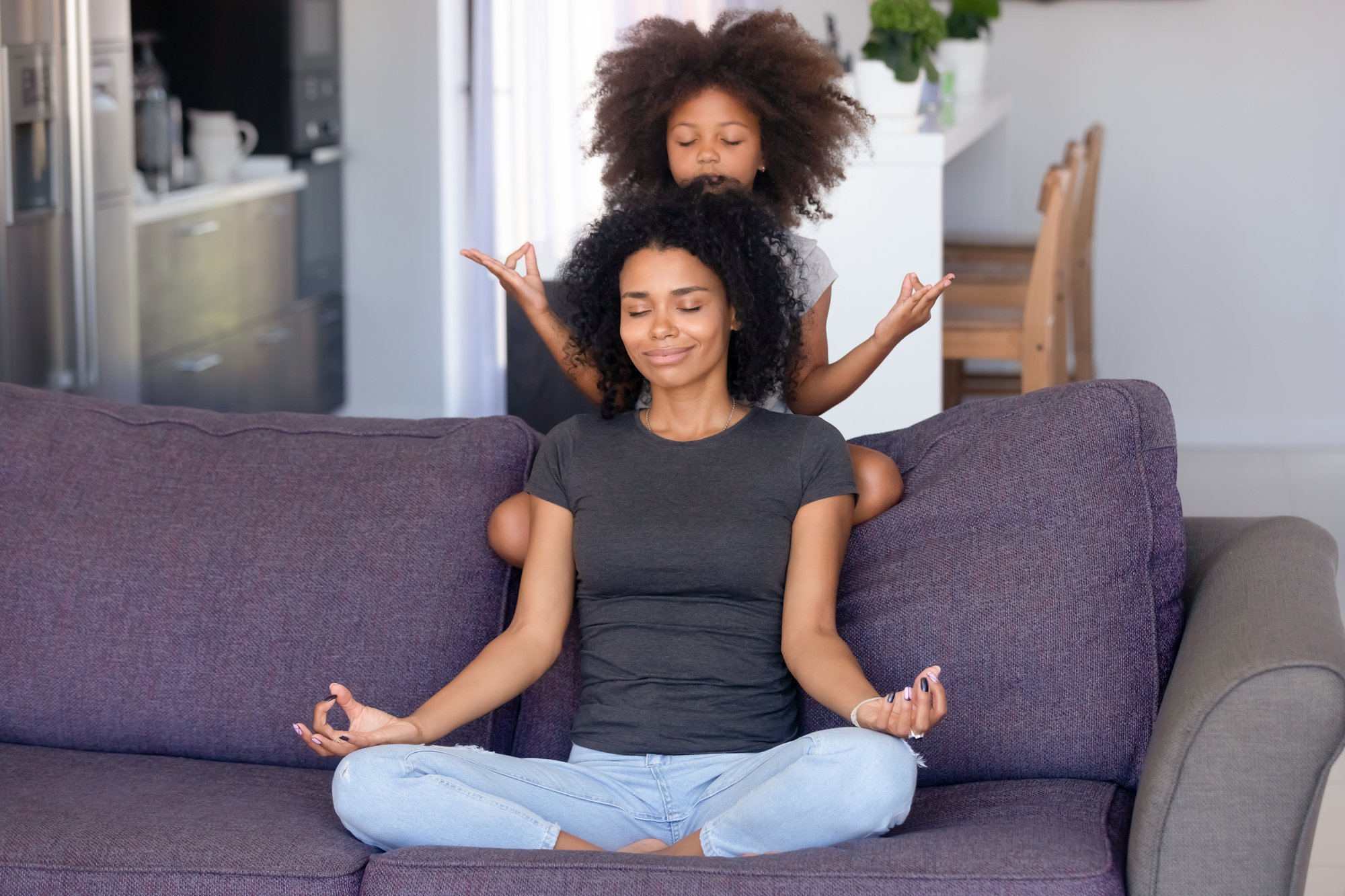 African mother and little daughter meditating on couch at home