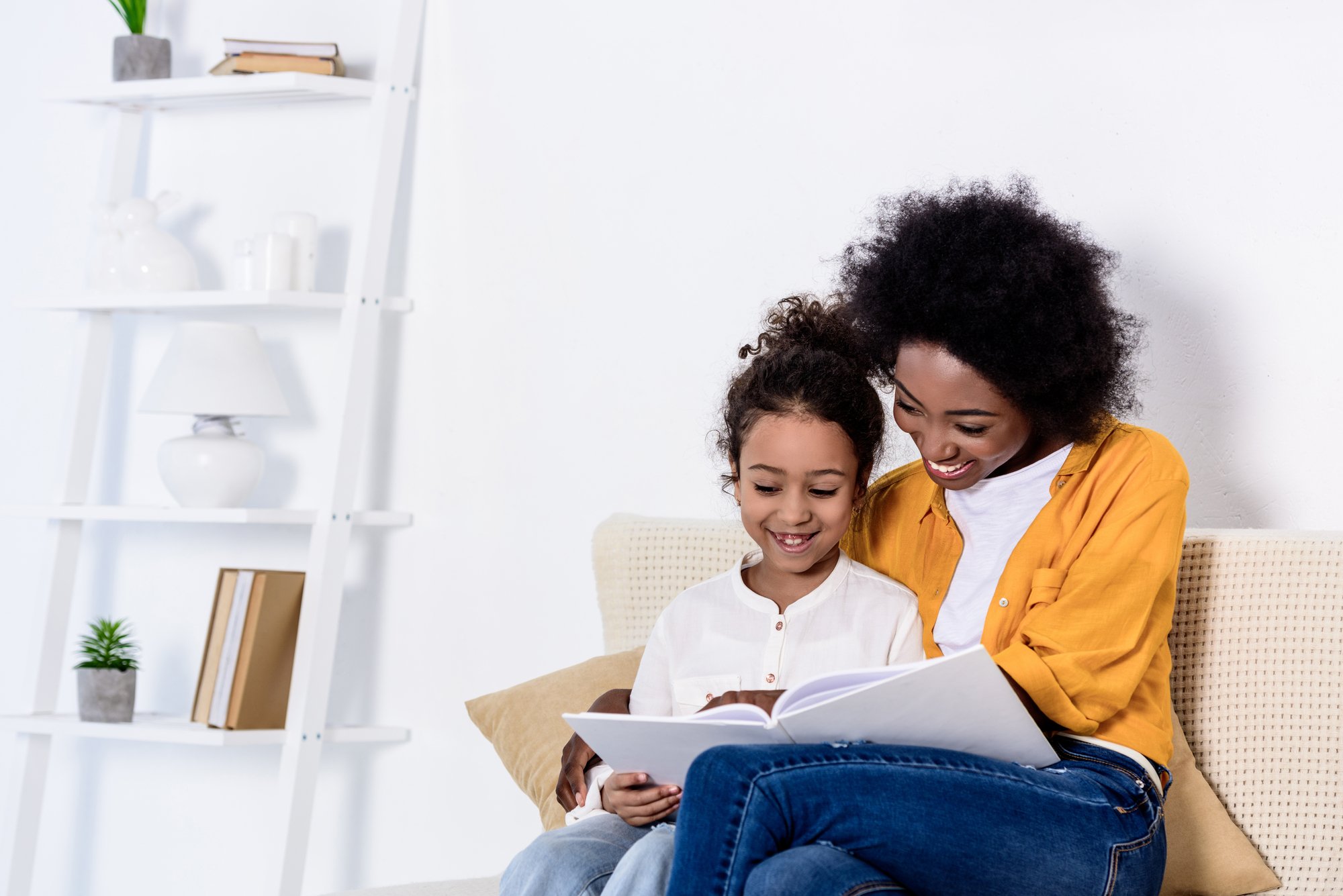 Happy african american mother and daughter reading book together at home
