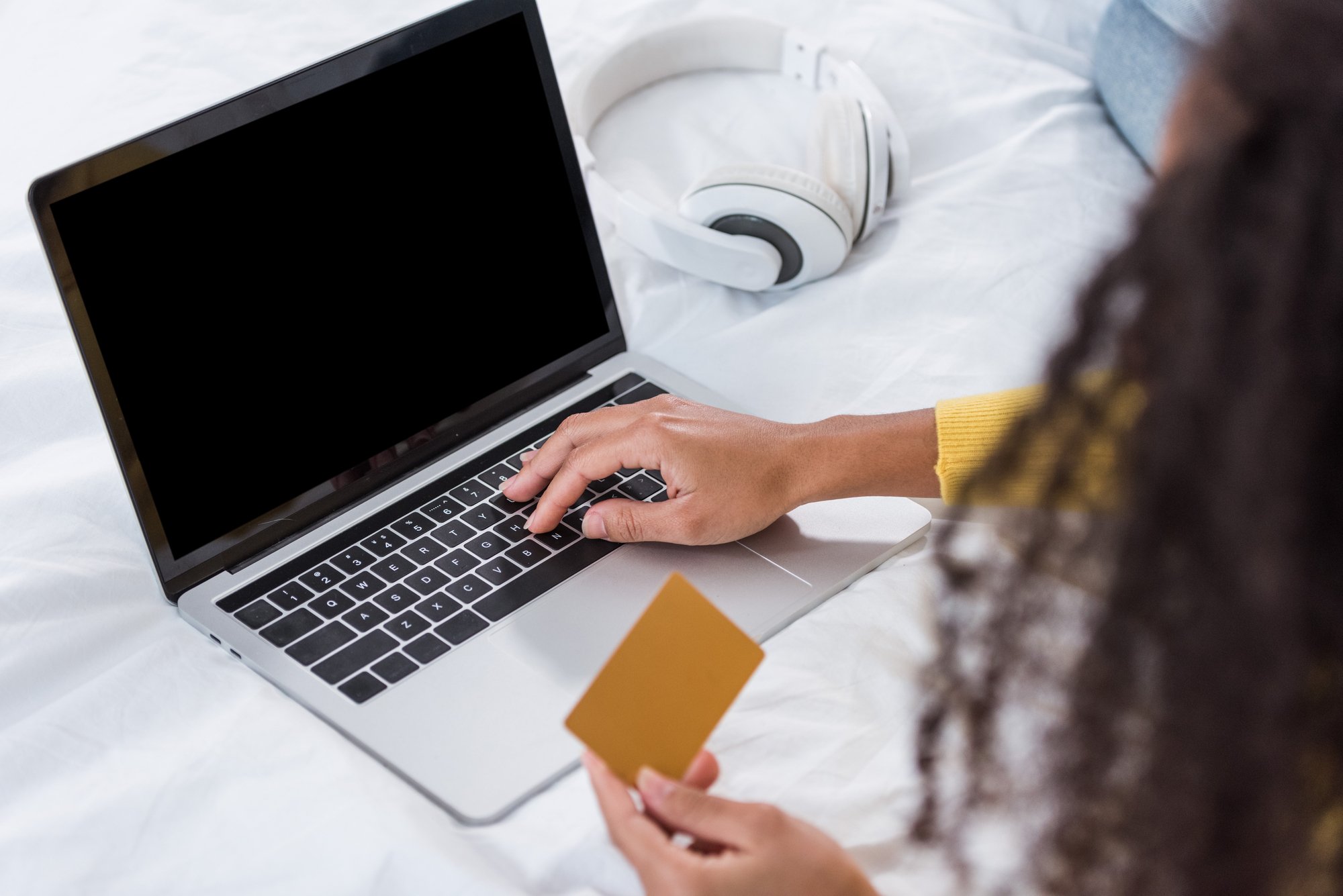 Partial view of woman holding credit card and doing online shopping on laptop in bed at home
