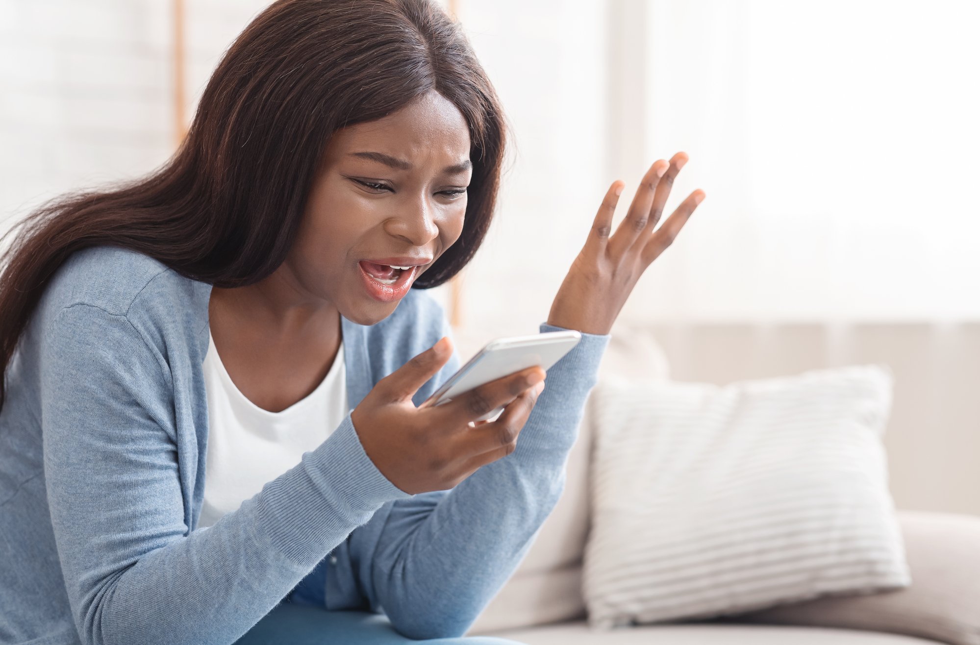 Portrait of young black woman shouting at mobile phone at home