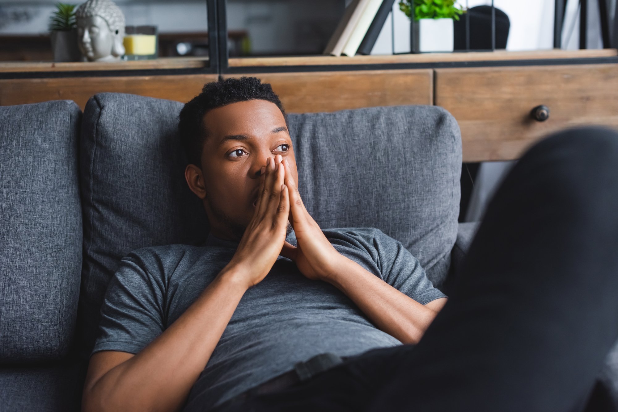 Sad thoughtful african american man lying on sofa at home