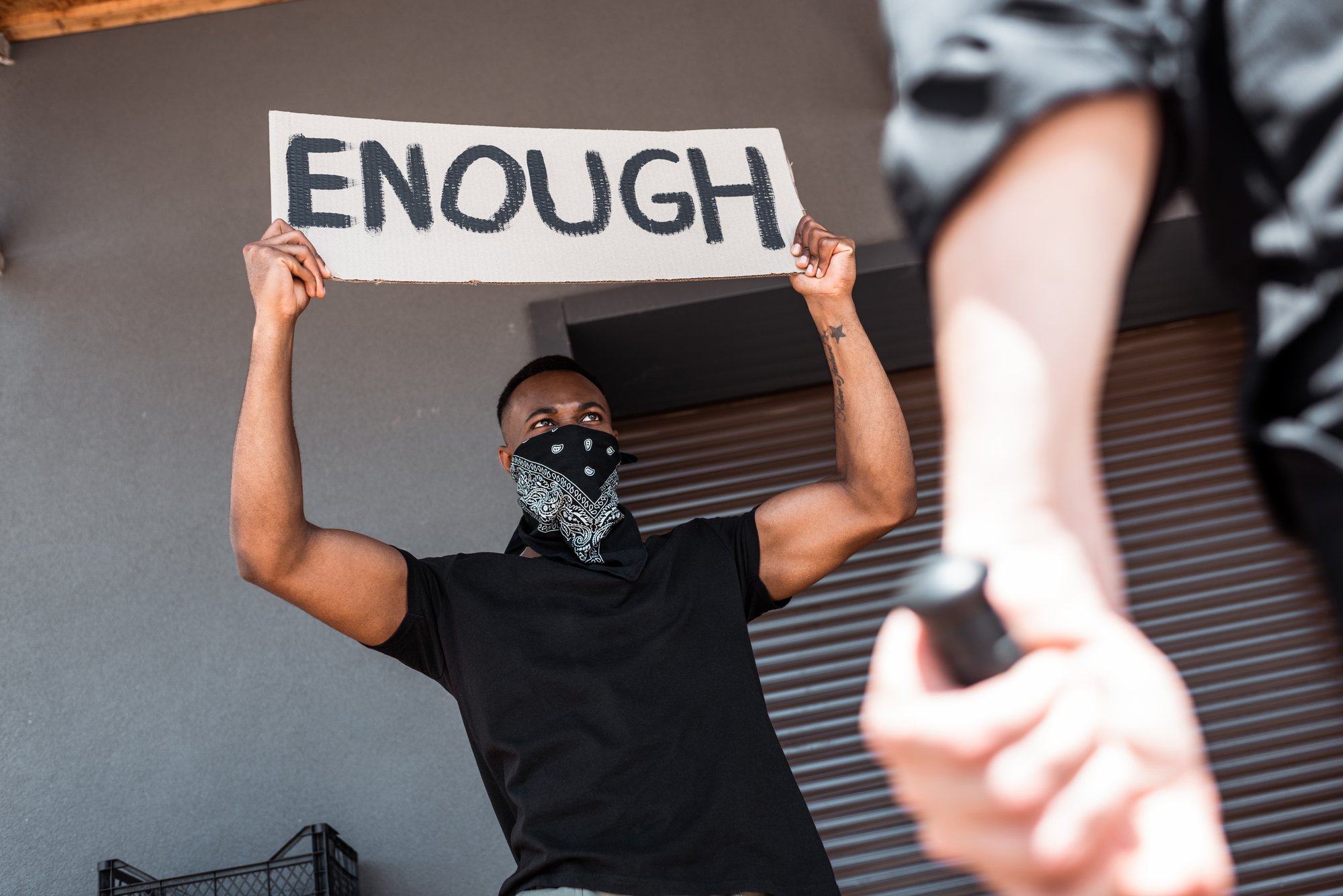 Selective focus of african american man with scarf on face holding placard with enough lettering near policeman with truncheon, racism