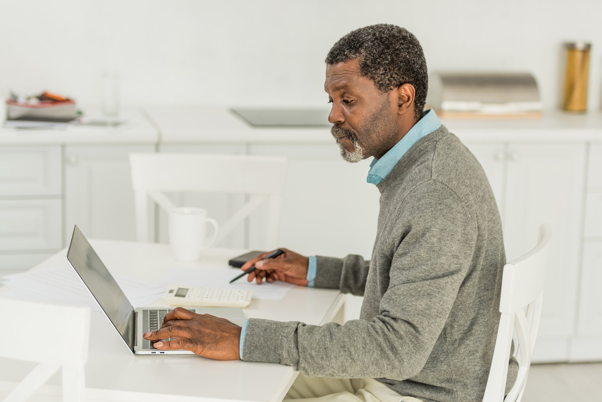 Serious african american man using laptop while calculating expenses