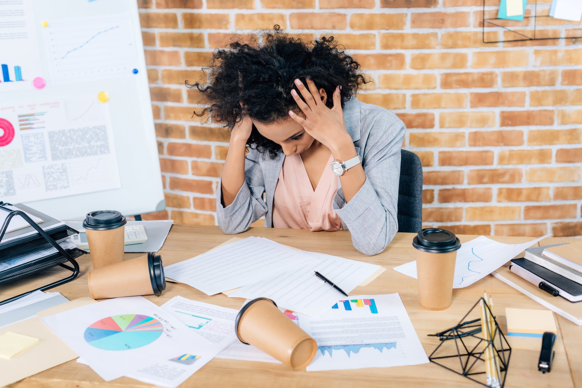 Stressed african american Casual businesswoman at desk with coffee to go cups and charts in office