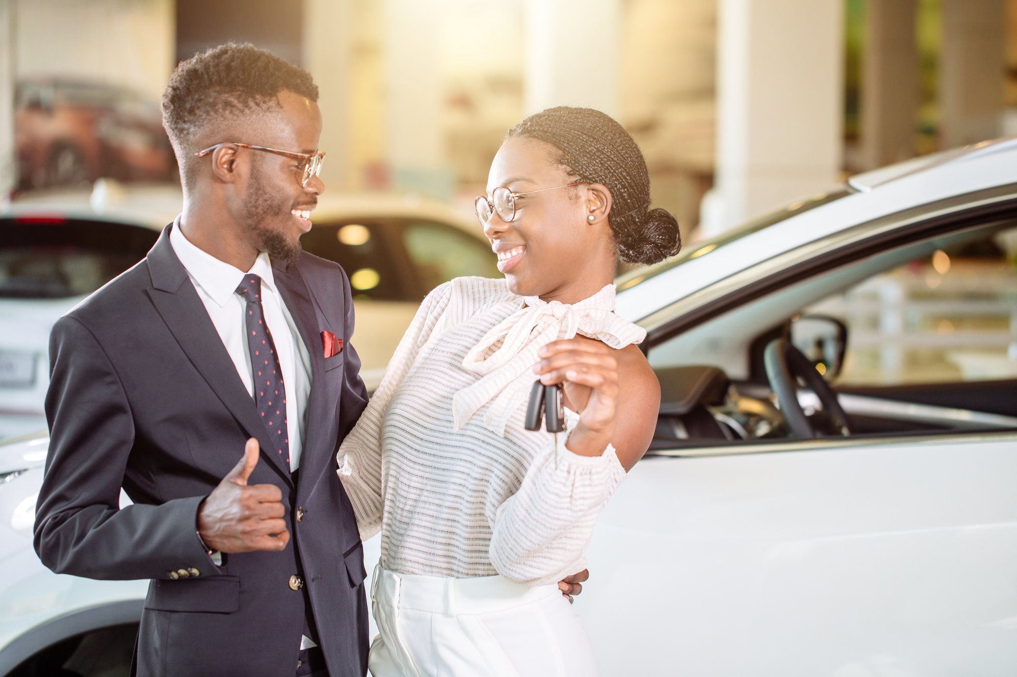 Visiting car dealership. couple holding key of their new car, looking at camera